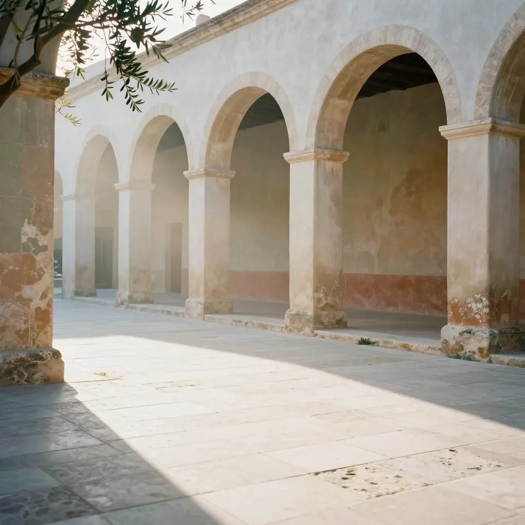 Loggia mediterranea con archi chiari, soglia in pietra e rami d’ulivo in luce calda.